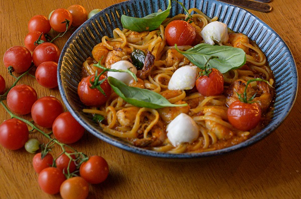 paste cu sos de rosii, cu bucatele de peste din conserva, cu mozzarella proaspata si cu busuioc intr-un castron albastru, langa castron aflandu-se un vrej cu rosii cherry