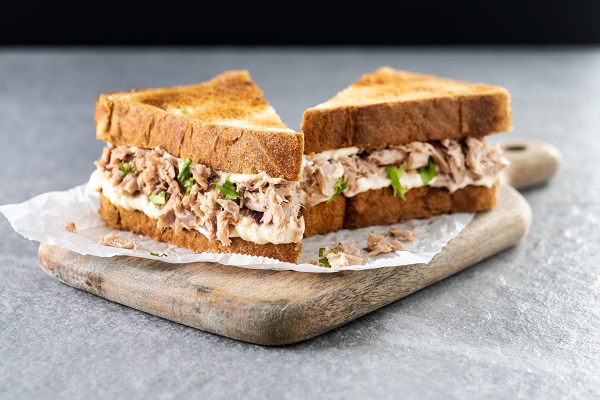 sandvisuri cu paine prajita taiata triunghi cu pasta de peste amestecata cu verdeata puse pe o bucata de hartie de copt de pe un tocator de lemn