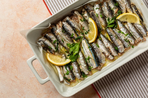 sardine la cuptor, cu lamaie si patrunjel proaspat, puse intr-o tava alba, asezata pe un prosop de bucatarie alb cu dungi gri