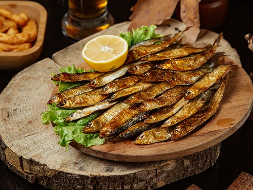 pesti preparati pe gratar sau la cuptor, cu lamaie si salata verde,pusi pe un tocator de lemn pus, la randul sau,pe un tocator de lemn rustic, similar cu o buturuga, pe fundal sesizandu-se un castron cu peste prajit, un pahar de bere si o frunza de toamna