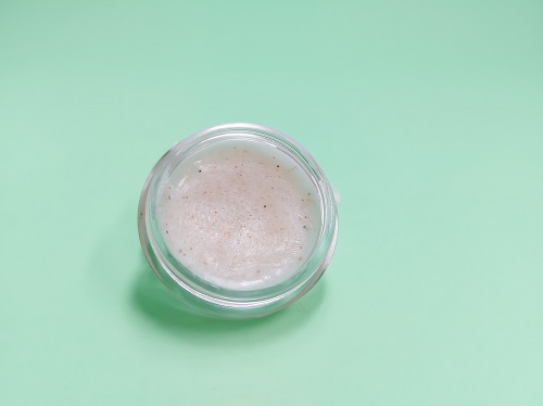 balsam de buze cu proprietati exfoliante, pus intr-un recipient de plastic sau de sticla, pe fundal vernil