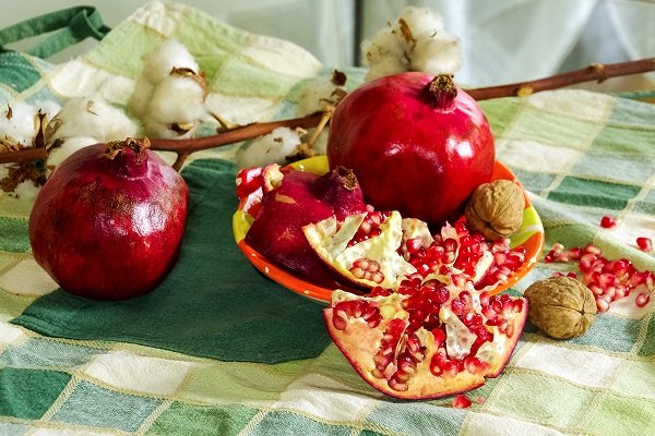bumbac, doua rodii intregi, jumatati de rodie si nuci asezate pe un prosop de bucatarie cu carouri bej si in diverse nuante de verde