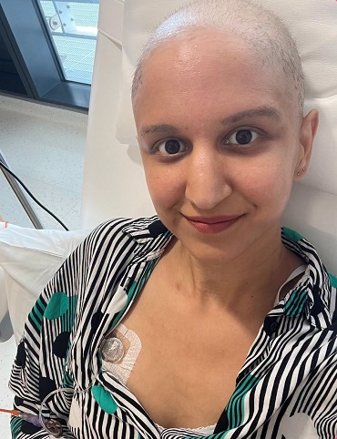 Meera Kotecha, mama de 37 de ani diagnosticata cu cancer de san, fara par, aflata pe un pat de spital, imbracata cu bluza cu dungi albe si negre, in timpul unei sedinte de chimioterapie