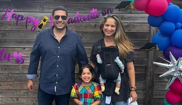 Meera Kotecha, diagnosticata cu cancer de san la 37 de ani, imbracata cu bluza neagra cu buline albe si cu blugi, zambitoare alaturi de sotul ei, care poarta ochelari de soare, dar si de copiii ei, o fetita cu rochita colorata in carouri si un baietel pe care il Meera ill tine intr-un marsupiu, toti patru la o petrecere cu baloane si cu ornamente argintii 