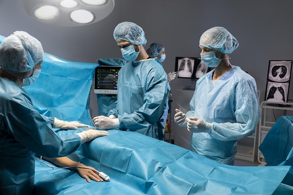 pacienta invelita cu camp chirurgical albastru pregatita pentru o interventie chirurgicala in timp ce echipa medicala se afla langa ea
