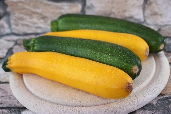 doua sortimente de zucchini proaspeti, asezati pe un tocator de lemn rotund, pus pe o suprafata de piatra