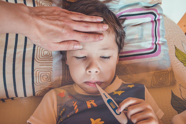 copil care sta in pat cu termometrul in gura