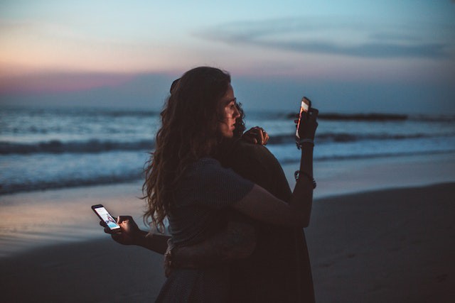 cuplu pe plaja cu telefonul in manaî