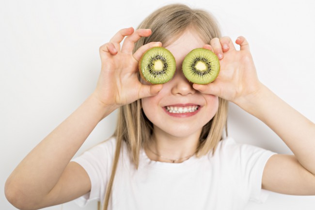 copil care tine in dreptul ochilor doua bucati de kiwi