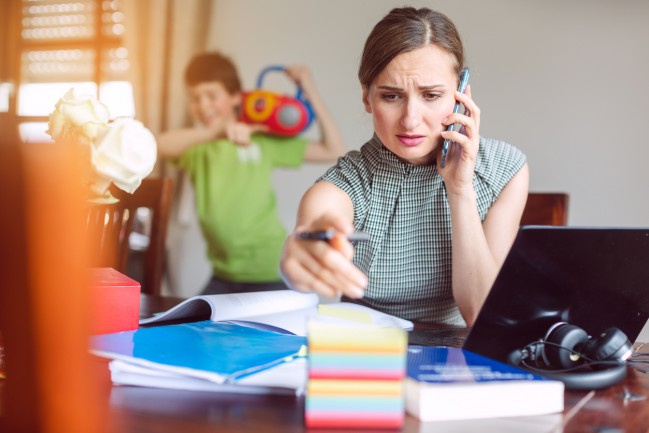 mama stresata care lucreaza de acasa si copilul care se joaca in spatele ei