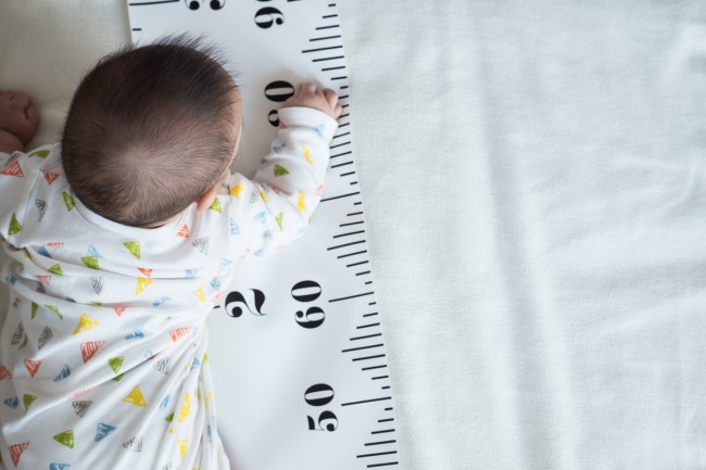 bebelus care sta pe burta pe pat langa un centimetru