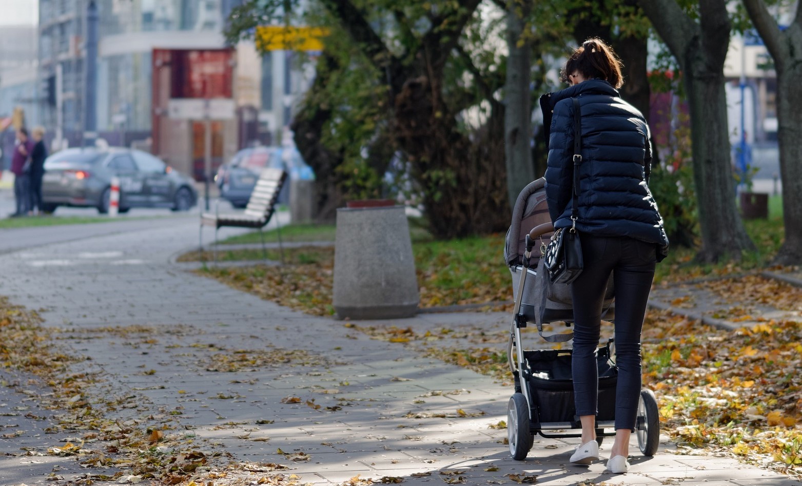 o mama care isi plimba bebelusul in carucior pe strada