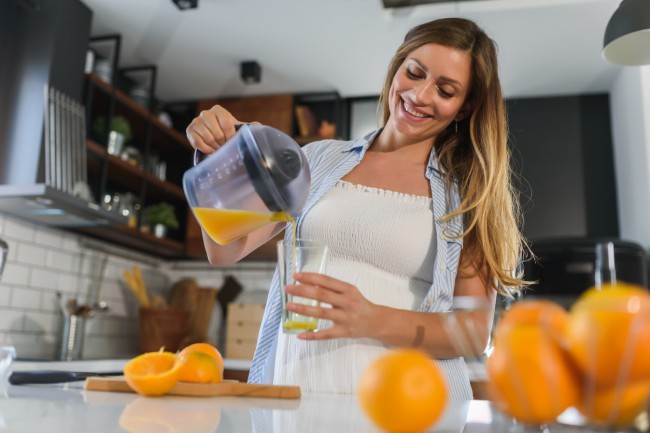 femeie insarcinata care isi toarna suc de portocale in pahar
