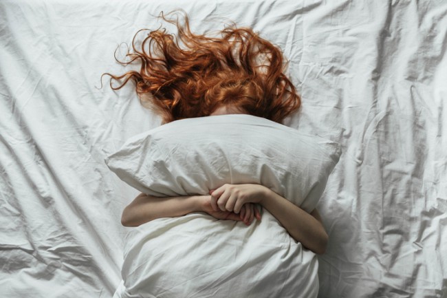femeie cu par roscat care sta in pat cu o perna pe corp
