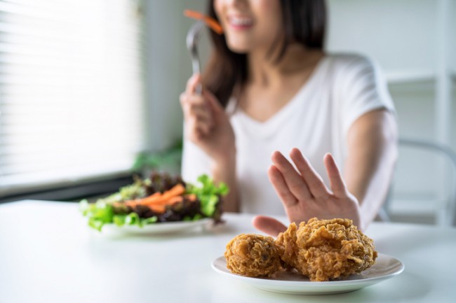 femeie care mananca o salata si refuza o farfurie cu aripioare picante