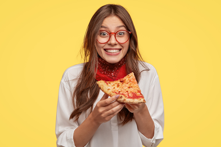 femeie cu ochelari de vedere care tine in maini o felie de pizza