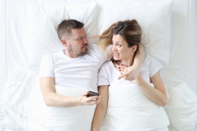 Bărbat supărat care tine in mainile sale telefonul mobil al sotiei sale, in timp ce se afla in pat