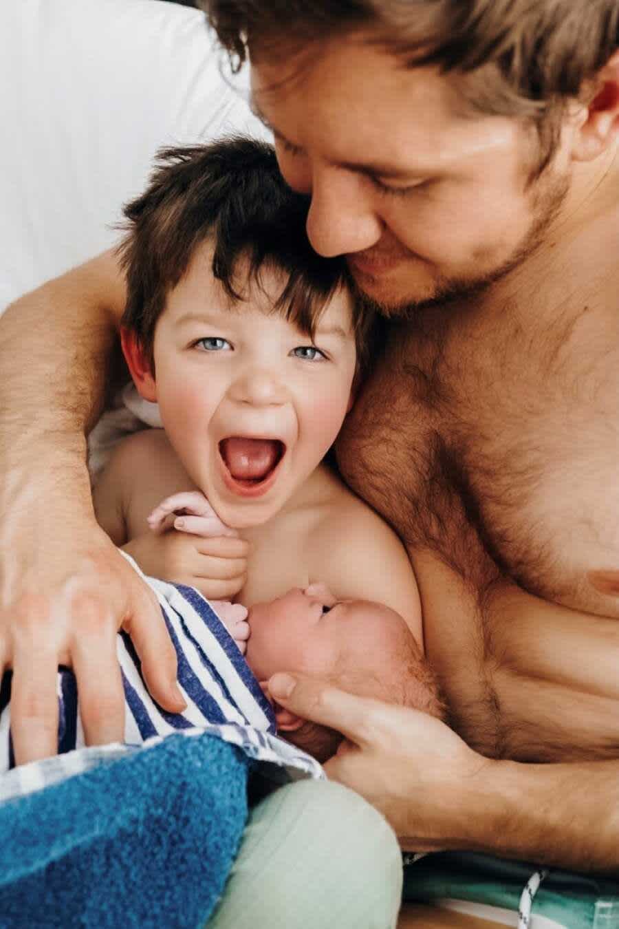 baietel care rade in timp ce tine in brate un bebelus