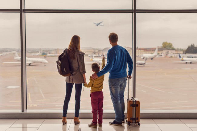 doi parinti cu copilul la aeroport, uitandu-se la cum decoleaza un avion