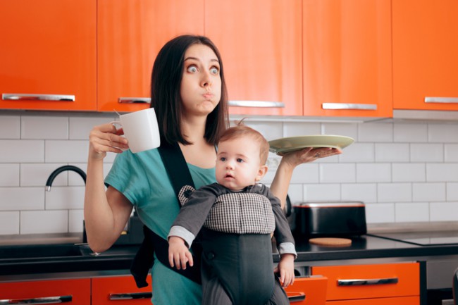 Mamă multitasking ocupată cu bebelușul, cană de cafea și veselă