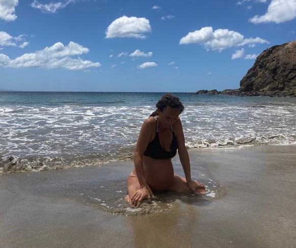 femeie insarcinata care sta in genunchi pe malul oceanului