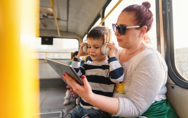 mama cu copilul cu tableta si casti intr-un mijloc de transport in comun