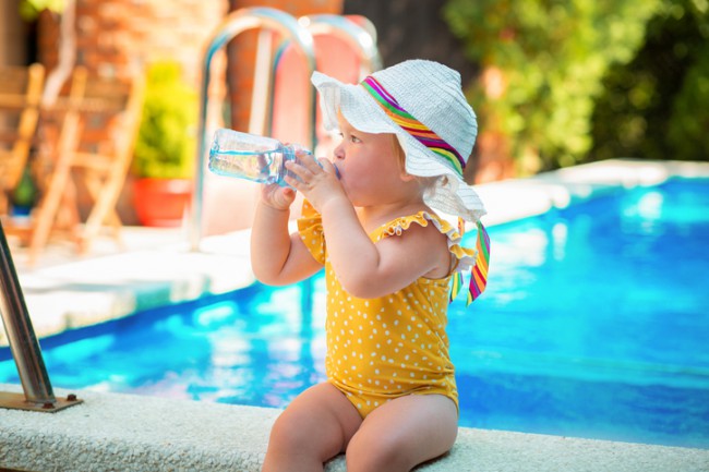 bebelus in costum de baie care bea apa la marginea piscinei