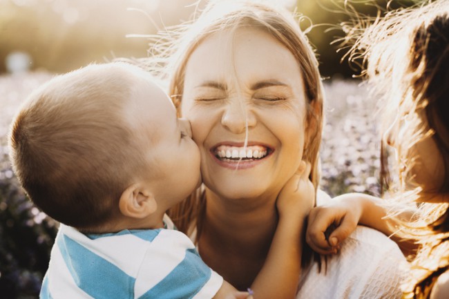 mamă care râde cu ochii închiși în timp ce fiul ei o îmbrățișează și o sărută pe obraz