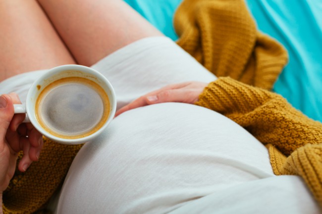 femeie insarcinata care tine in mana o ceasca cu cafea