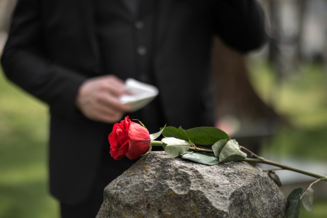 barbat care pune un trandafir pe o piatra funerara