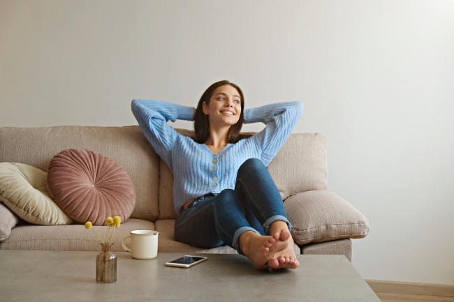 femeie tanara care se relaxeaza pe canapea, cu picioarele pe masuta de cafea