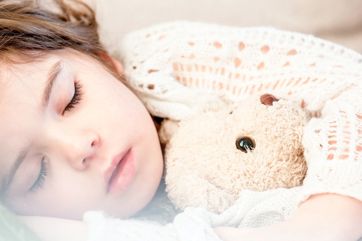copil care doarme linistit cu ursulet de plus in brate