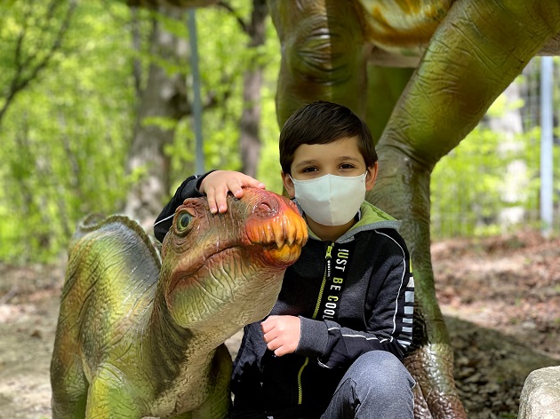 copil cu masca de protectie langa un dinozaur de jucarie