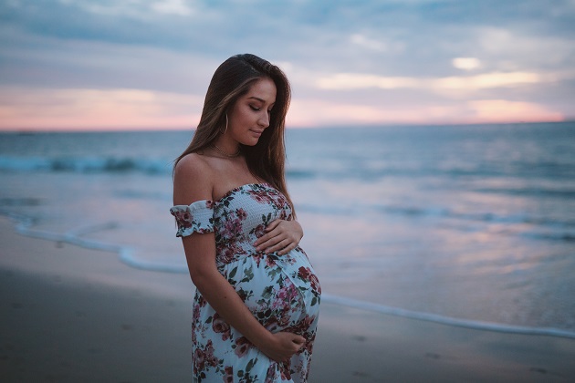 femeie insarcinata care sta la malul marii cu mainile pe burtica