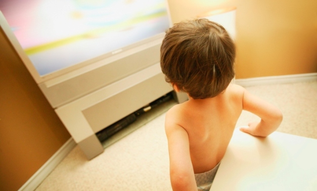 copil care se uita la televizor sprijinit de canapea