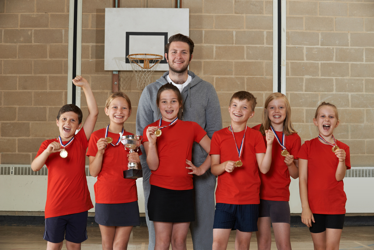 echipa de copii sportivi cu antrenorul tinand medalii in maini
