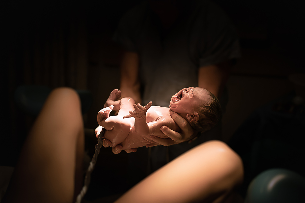 Nou-nascut la nastere naturala cu cordon ombilical atasat tinut in maini de medic