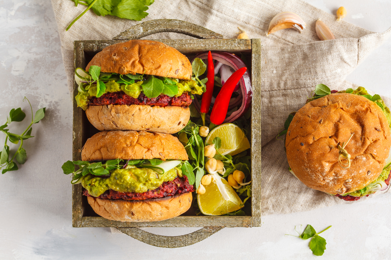 burgeri vegetali cu fasole rosie, sos de avocado, salata langa boabe de naut si bucati de lamaie asezati intr-o tava de lemn