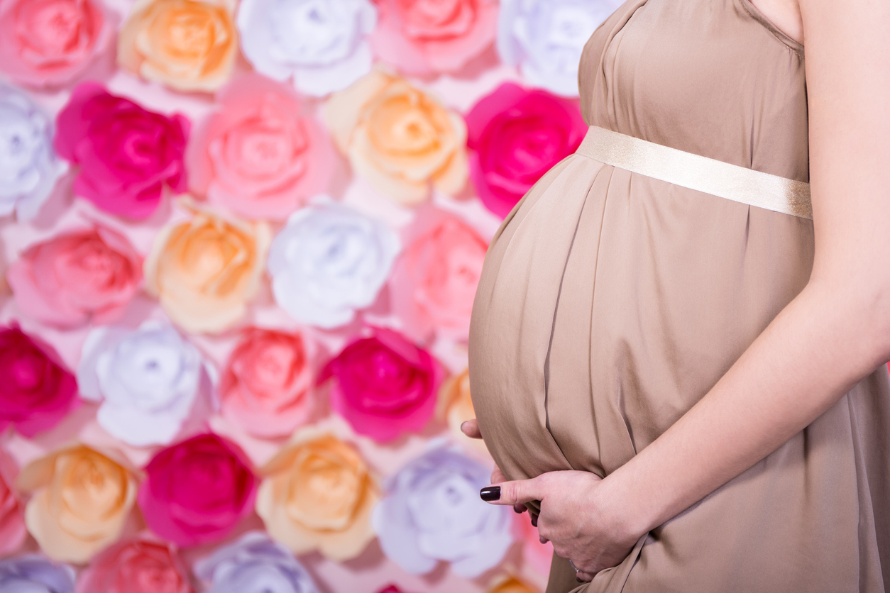 femeie gravida imbracata in rochie crem pe un fundal de flori