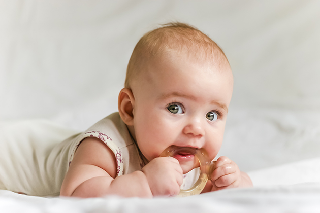 bebelus cu jucarie de dentitie in gura stand pe burta