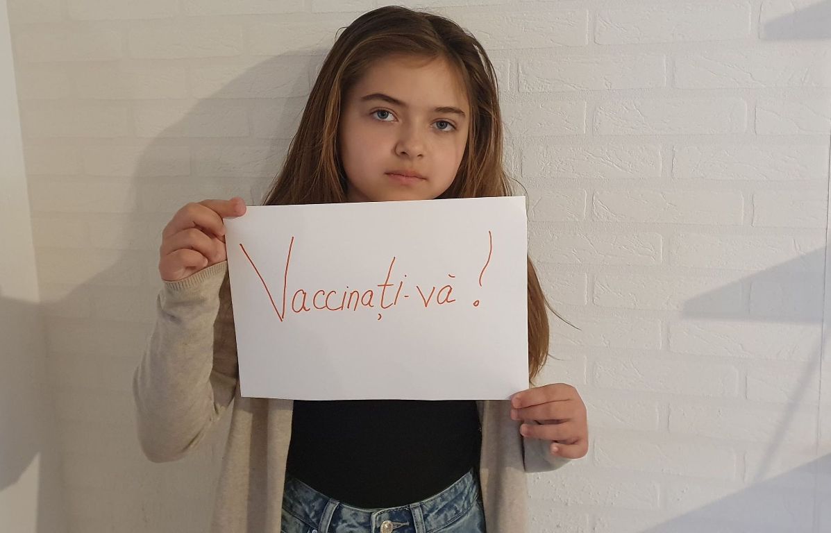 fetita cu o hartie in mana pe care scrie vaccinati-va