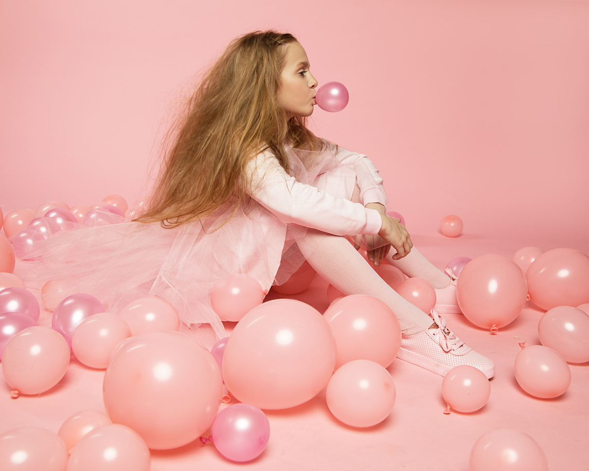 o fata care sta pe jos printre baloane roz imbracat in rochie roz