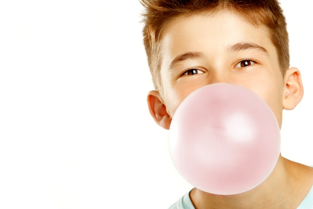 copil care face un balon roz din guma de mestecat