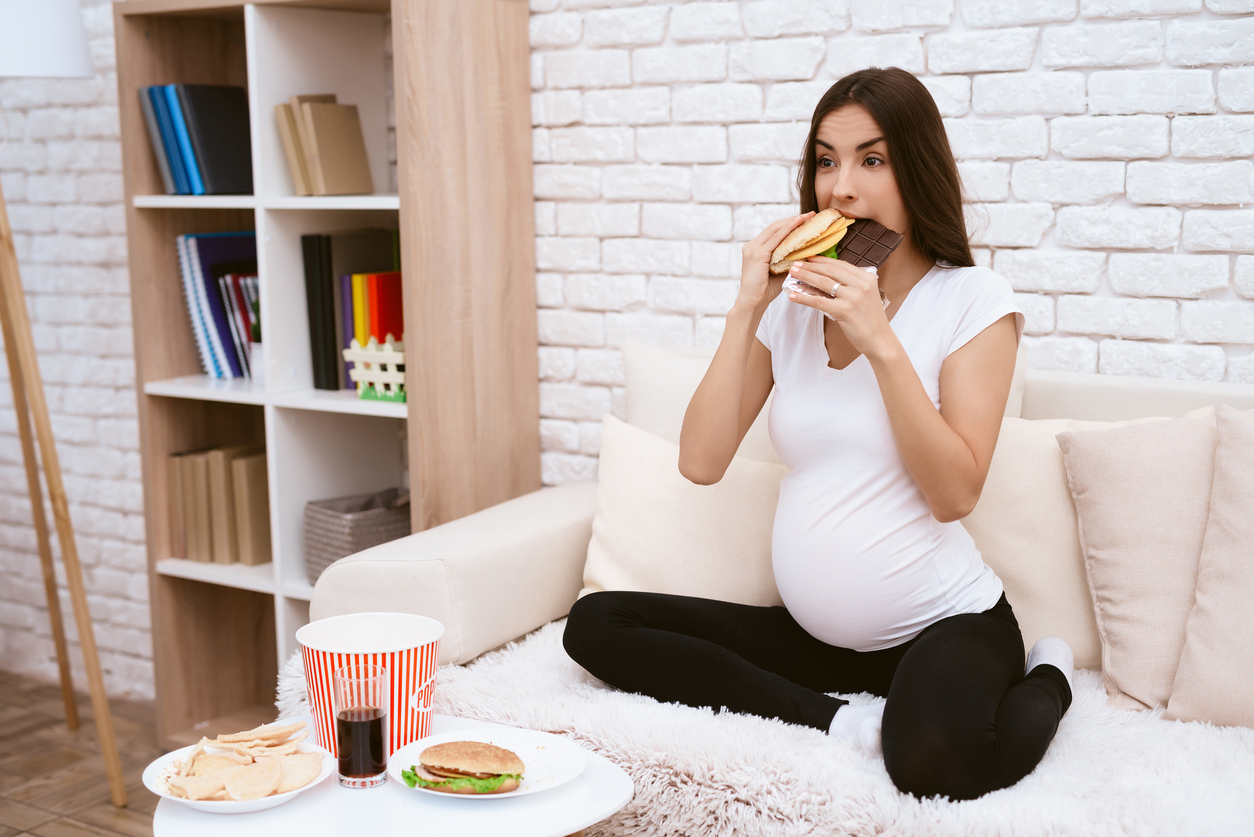 femeie gravida care mananca cu pofta un burger