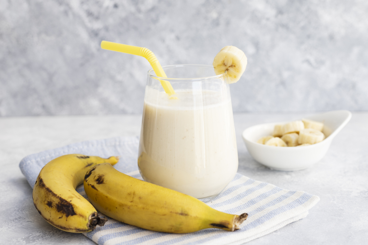 smoothie de banana intr-un pahar transparent cu banane langa