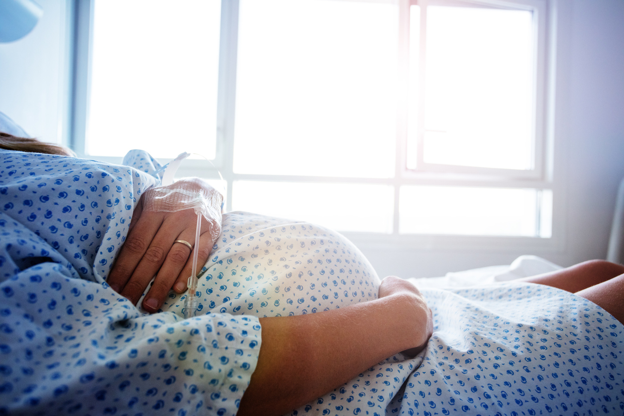 femeie insarcinata pe un pat de spital tinandu-si burta