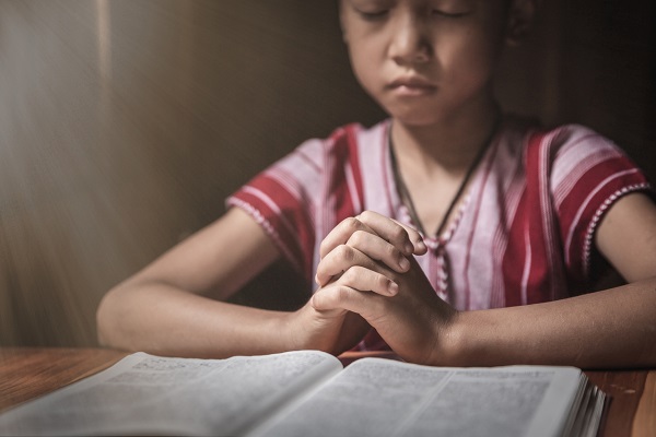fata care se roaga cu mana pe carte de rugaciuni