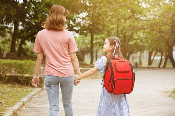 mama cu fata de mana si ghiozdan rosu in spate pe alee