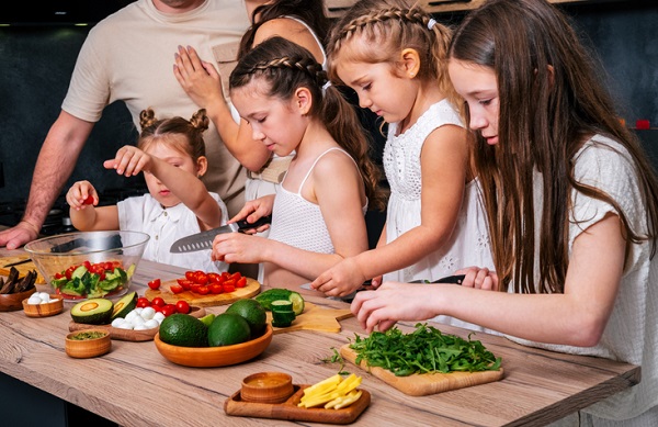 patru fete pregatesc salata sub supravegherea unui adult