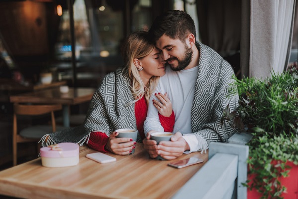 cuplu tandrete la masa in fata unei cesti de cafea